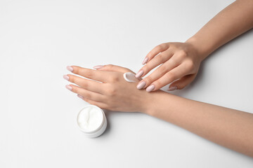 Woman with beautiful manicure applying cream on white background, closeup