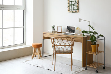 Modern workplace with blank frame and laptop near light wall