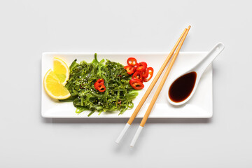 Plate with healthy seaweed salad, chili pepper and lemon on light background