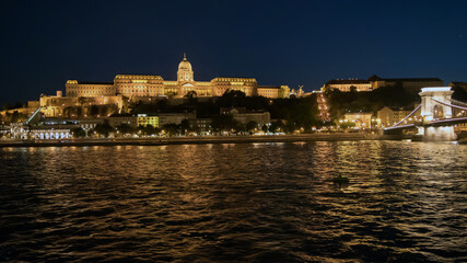 Fototapeta premium Buda Castle glows in the night overlooking the Danube River and Chain Bridge in Budapest, Hungary.