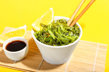 Bowl with healthy seaweed salad on yellow background