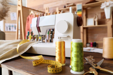 Thread spools with measuring tape and tailor's scissors on table in atelier, closeup