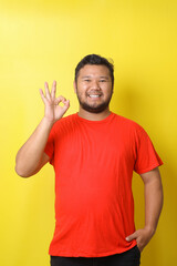 Excited Asian man in basic clothing smiling and showing ok sign at camera isolated over yellow background
