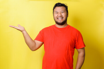 Young Asian fat man wearing casual clothes with a big smile on face, pointing with hand and finger to the side looking at the camera.