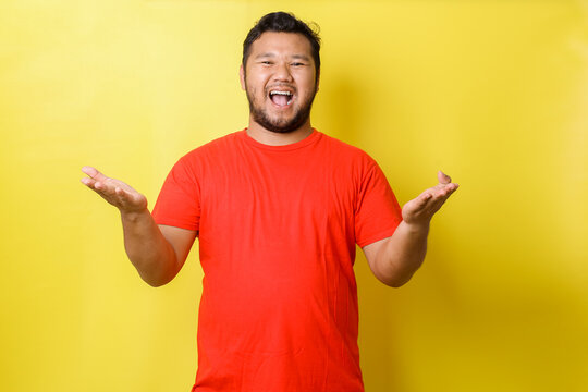 Funny attractive guy in red t-shirt hold open palms hands advertising two new popular products low prices shopping, isolated over yellow background
