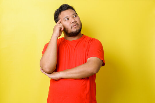 Young Asian Fat Man In Red T Shirt Thinking About Things, Isolated On Yellow Background