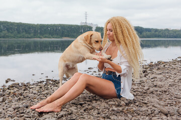 Young woman sitting with her labrador retriever dog on the river shore