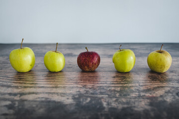 group of green apples with one red apple in the middle, healthy food or metaphor of standing out from the crowd