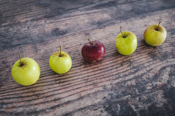 group of green apples with one red apple in the middle, healthy food or metaphor of standing out from the crowd