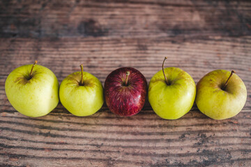 group of green apples with one red apple in the middle, healthy food or metaphor of standing out from the crowd