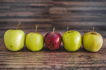 group of green apples with one red apple in the middle, healthy food or metaphor of standing out from the crowd