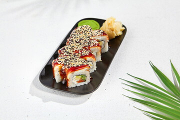 Trendy asian food - canada maki on black plate on white concrete background. Sushi roll with eel and unagi sauce outside, cheese, salmon and cucumber inside. Maki sushi with eel.