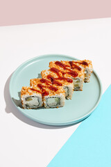 Sushi roll with chicken, cucumber and cheese inside, crispy onion outside. Maki sushi with chicken on ceramic dish. Alternative maki sushi  on coloured background in minimal style. Sushi no fish.