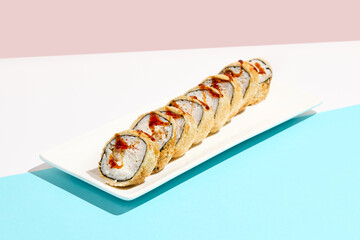 Tempura maki roll with shrimps and unagi sauce. Hot sushi with shrimps, cheese and crab  inside, unagi sauce topped. Modern japanese menu concept. Maki sushi on coloured background.