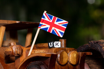 Mote alphabet blocks arranged into "UK" on a miniature wooden car and the national flag.