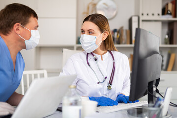 Young female therapist consulting with male colleague while working on laptop in medical office