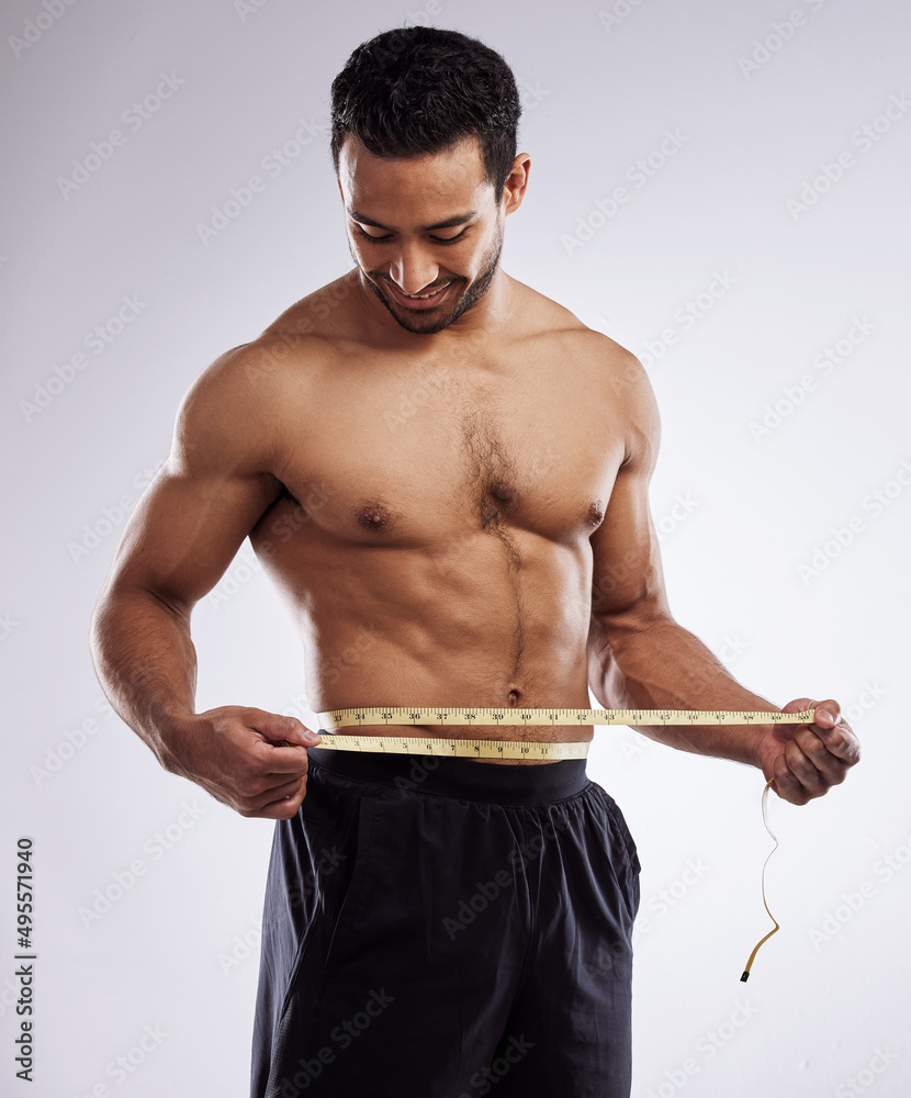 Poster almost at my ideal weight. shot of a man measuring his waist using a measuring tape against a studio