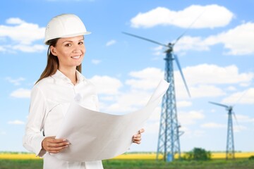 Beautiful man in white helmet working with digital tablet at energy farm. Male inspector controlling functioning of wind turbines outdoors.