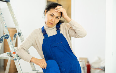 Portrait of tired Asian woman builder standing in apartment.