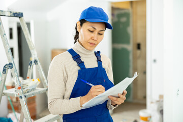Female Asian engineer writing in check list during repair works in house.