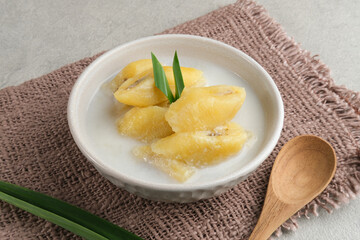Kolak, Kolak Pisang is Indonesian traditional dessert, very popular during Ramadhan, made from banana with coconut milk, sugar and pandanus leaves. Served in white bowl on grey background, copy space.