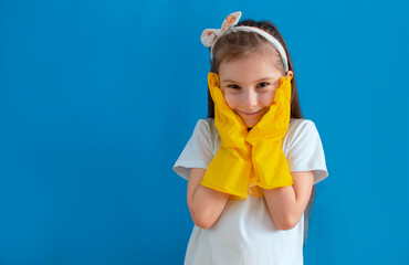 Smiling charming little housewife girl with a surprised face in rubber gloves for washing, cleaning, doing homework, isolated on a blue background. The concept of household management