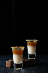 Alcoholic shots with coconut liqueur and whiskey on a black background, close-up