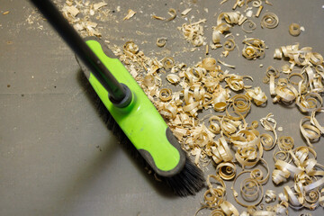 a small pile of wood shavings on a gray linoleum floor with a broom brush