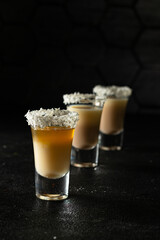 Alcoholic shots with coconut liqueur and whiskey, coconut chips, on a black background, close-up