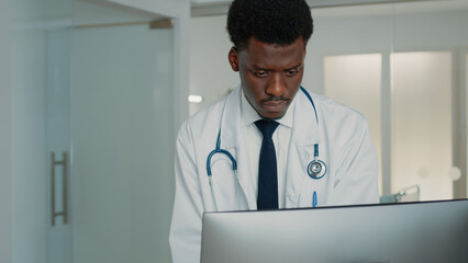 Man working as medic looking at computer to find information on healthcare treatment in hospital ward. Medical specialist with stethoscope and white coat using monitor to cure patient