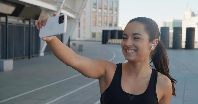 Fit woman runner making selfie photos on her smartphone after sport fitness training outdoors near stadium