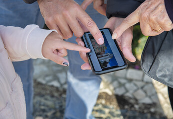 Searching for a city landmark outdoor. Fingers of many people touching the smartphone screen.