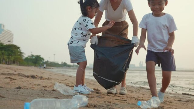 Volunteer happy family picking plastic bottle into trash plastic bag black for cleaning beach, Mother and his children clean up garbage at sunset, Ecology and World Environment Day, Save earth concept