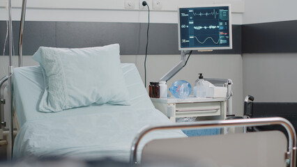 Close up of empty hospital ward bed with medical equipment. Emergency room with reanimation tools for healthcare, heart rate monitor and oxygen tube. Space for intensive care recovery