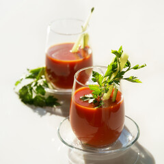 tomato juice with parsley and cucumber in glass glasses on a light background