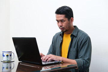 Adult Asian man showing serious expression when typing on his laptop