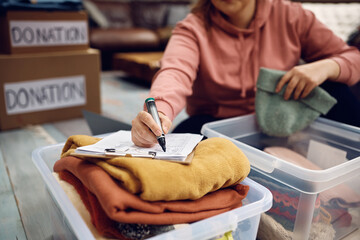 Close up of woman going through checklist while packing clothes into donation boxes.