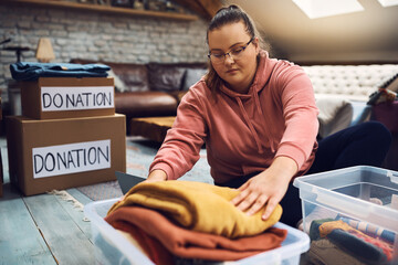 Young woman packing wardrobe into charitable donation boxes. - obrazy, fototapety, plakaty