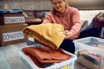 Close-up of woman sorting clothes while packing donation boxes for charity. - obrazy, fototapety, plakaty