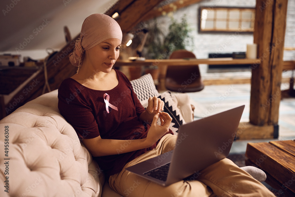 Wall mural woman with breast cancer makes video call over laptop while relaxing at home.