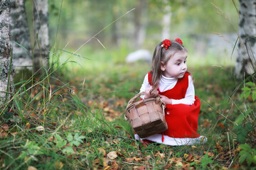 A little girl in a red hat and dresses is walking in the park. Cosplay for the fairytale hero 