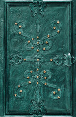 An old dark emerald green metal door with an openwork ornament. Vintage cracked background closeup....