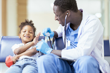 Fototapeta premium A young African girl sits for the doctor to check her health and plays with her mobile phone.