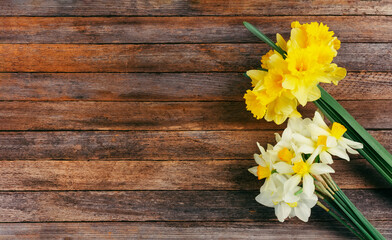 a bouquets of white and yellow narcissus flowers on a brown wooden background with a copy space
