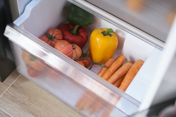 Tomatoes, peppers and carrots in the vegetable drawer of the opened fridge.