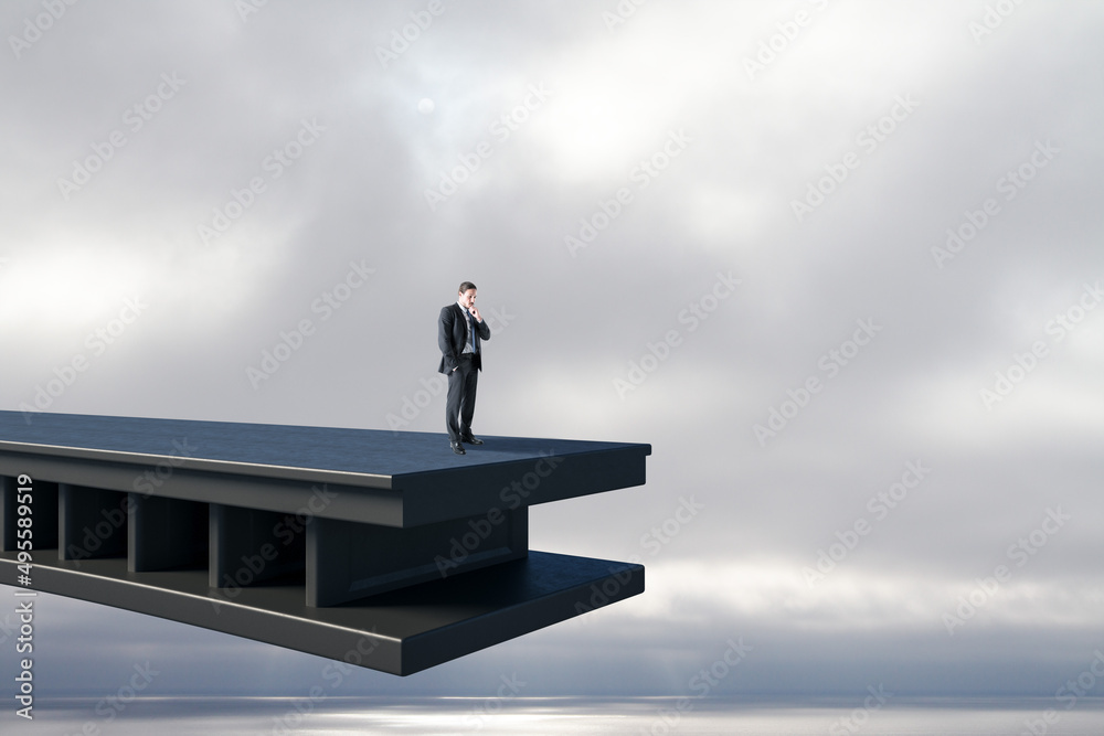 Poster Attractive pensive young business man standing on bridge with gap and dull sky background with mock up place. Challenge and obstacle concept.