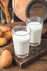 Two glasses of potato milk with raw potatoes on a brown background.