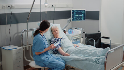 Nurse giving assistance to senior patient with disease in bed. Medical assistant and doctor doing...
