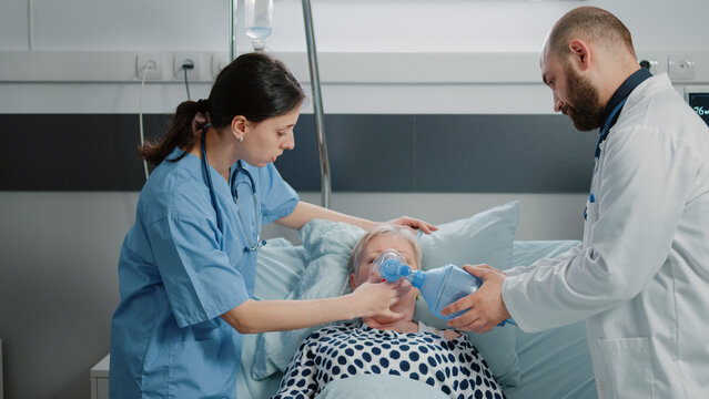 Sick woman asking for assistance from medical team in hospital ward bed. Doctor and nurse using oxygen tube and checking heart rate monitor for elder patient with respiratory problem.