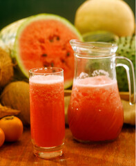 Fresh watermelon juice glass and jar on tropical fruits background.
